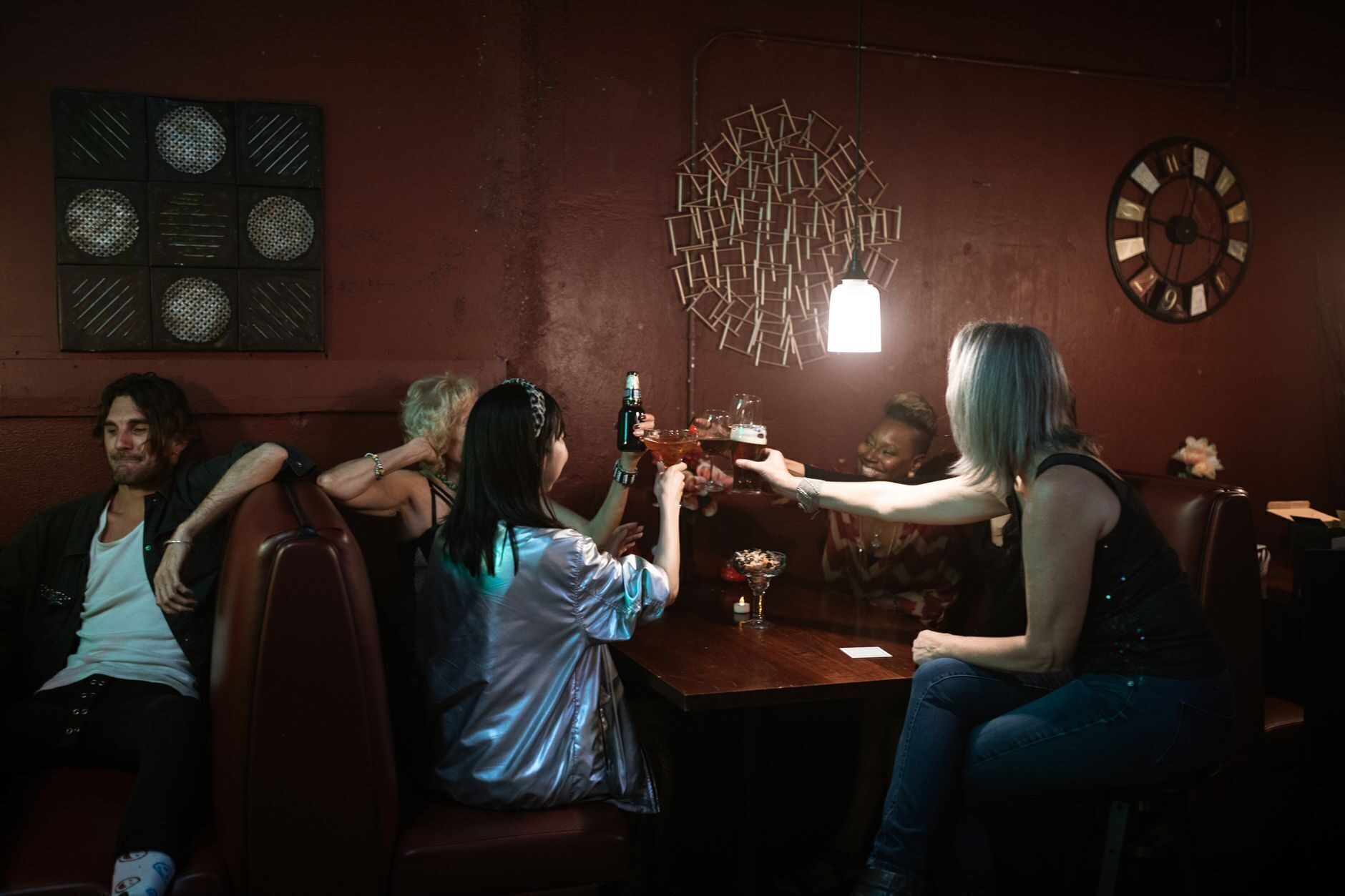 Four friends gathered around a dark table under a single overhead pendant, mid-story